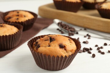 Delicious muffin with chocolate chips on white wooden table, closeup