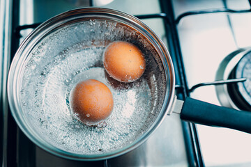 Saucepan stainless steel with two boiling eggs breakfast in a water on a gas stove top view.