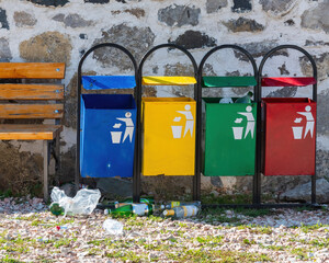 colorful metal garbage cans next to the bench, empty plastic bottles lying on the ground below. environmental pollution