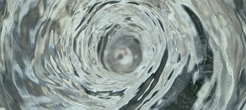 Water vortex swirling counterclockwise in slow-motion. The water is pulled down and forced toward the drain hole