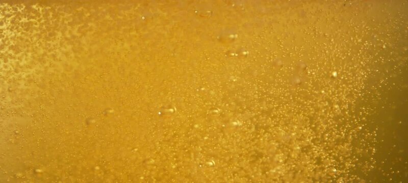 Golden beer pouring into glass with foam and many gas bubbles floating up in slow-motion. Close- up view