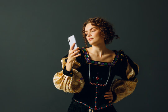 Portrait of a young aristocratic woman doing photo selfie with mobile phone and dressed in a medieval dress