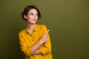 Confident young woman in yellow blouse making a pointing gesture while looking away against olive...