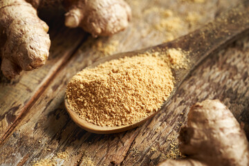 Ground ginger powder on a spoon with fresh ginger root