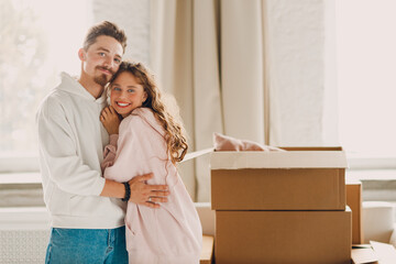 Happy young family couple man and woman hugging after moving cardboard boxes to their new apartment.