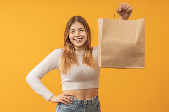 Woman with a cropped top showing a brown paper bag against a yellow background