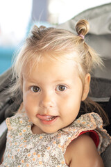 A young girl with blonde hair is sitting in a baby carriage. She has a smile with a tongue on her face.