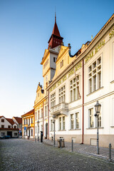 The historic Town Hall in Stara Boleslav stands proudly in the early morning light, showcasing its remarkable architecture along a quiet cobblestone street lined with trees.