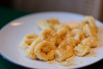 Crispy fried calamari rings on a plate with slices of lemon and parsley on a wooden boards background. High quality photo