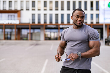 Muscular man in casual attire outdoors. A muscular man stands confidently outside a modern...