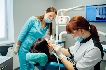 Dentist treats patient in clinic. Two dental professionals assist a patient during an oral...
