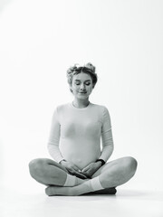 Pregnant woman doing yoga. A woman in a bright studio sits cross-legged, practicing yoga and focusing on mindfulness while pregnant.