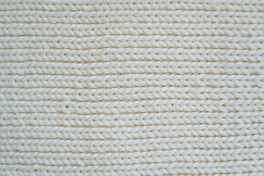 white texture of knitted wool fabric as a background, white smooth symmetrical lines of hand-knitted needlework pattern	
