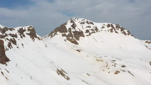4K aerial drone footage of the snow-covered summits of Mount Aragats, the highest peak in Armenia, with its crater in spring. Breathtaking views of rugged highlands, glaciers, and remote wilderness.