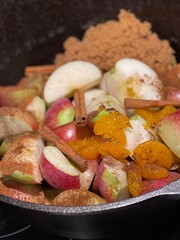 Homemade Apple Cider Making, with Fresh Apple Slices, Cinnamon Stocks, Ground Cinnamon, Nutmeg, Orange Slices, and Brown Sugar inside of a Large Cast Iron Dutch Oven.
