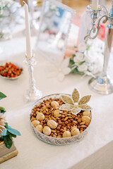 Dish with nuts decorated with a flower made from seeds is on the table near the candles. Tradition of Sofreh Aghd