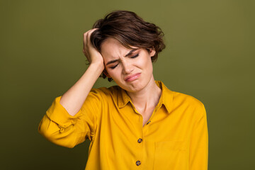 Upset young woman in yellow shirt expressing frustration with hand on head against green...