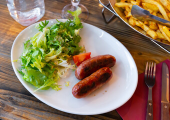 Appetizing fried sausages served with potatoes and salad on platter