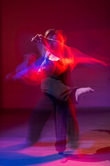 Fototapeta premium A young woman dances contemporary dances in blue and red light. Long exposure. Vertical photo. 