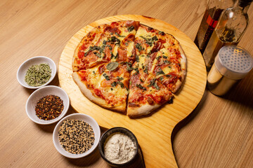 pizza grande cortada y  colocada sobre una bandeja de madera con 4 cuencos con ingredientes de adorno