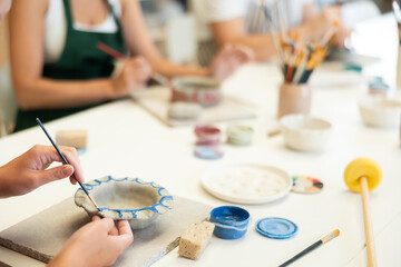Close up of female hands painting ceramic plate with paint and brush in pottery workshop