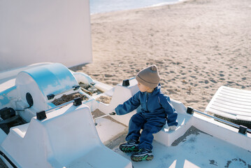 Little girl sits on a catamaran touching handles on a sandy beach