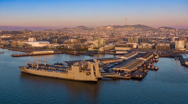 Aerial view of a large cargo ship docked in San Francisco Bay, alongside city skyline. Ships and docks are busy. Mission Bay, San Francisco, California, USA