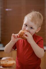 A young child in a red shirt enjoys a traditional Polish paczek, biting into its soft, glazed dough. The sweet treat, often eaten on Fat Thursday, symbolizes indulgence and festive celebration.