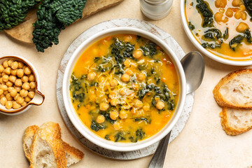 Healthy Homemade chickpea soup with kale, carrots, celery, onion, sweet potato.   Served with parmesan cheese and Bread.  Beige table surface.