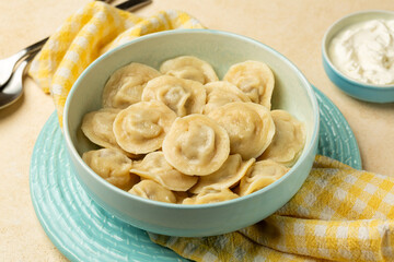 Homemade meat dumplings pelmeni in a light blue bowl and Sour cream.