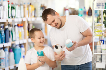 Young man with his son buyers chooses shampoo or shower gel in household chemicals store..