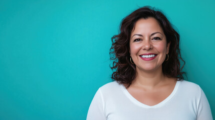 Fototapeta premium Hispanic Woman in Her 40s Smiling Warmly While Standing Against a Solid Turquoise Background, Exuding Confidence, Happiness, and Approachability