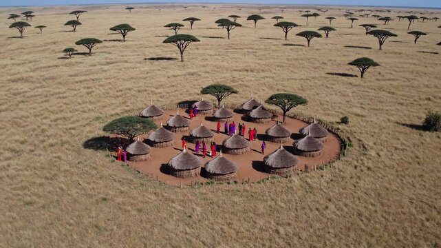 Aerial video captures a traditional village with thatched huts and people in colorful attire, set in a vast savannah landscape with scattered trees.