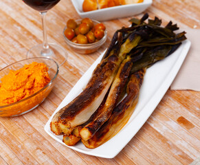 On rectangular plate -bunch of fried sweet green onions kalsot, supplemented with jar of romesco sauce,red wine,olives and white bread