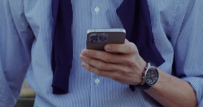 A businessman uses a mobile phone while standing in the city. Close-up of his hands