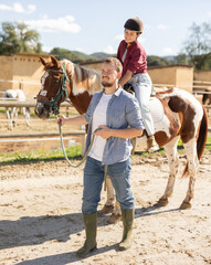 Young man leads horse on leash with young woman rider in paddock