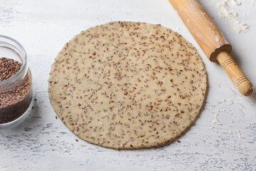 Raw vegan dough with flax seeds rolled out with a wooden rolling pin on a light blue background. Healthy homemade food concept