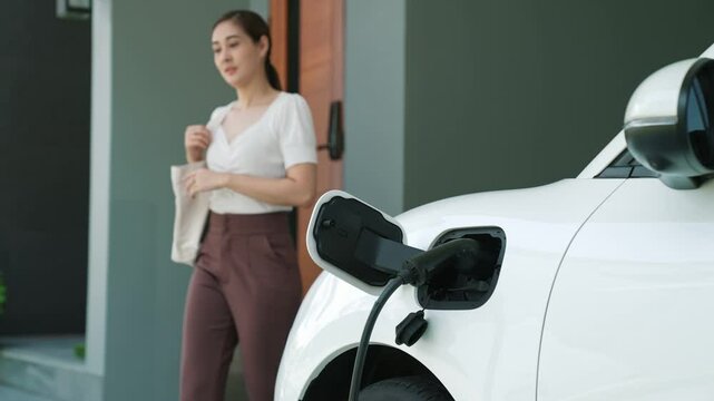 A woman unplugs the electric vehicle's charger at his residence. Concept of the use of electric vehicles in a progressive lifestyle contributes to a clean and healthy environment.