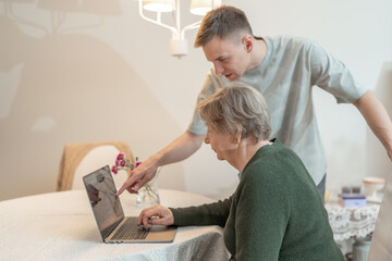 Young man helping an elderly woman with a smartphone at home. Concept of technology, education, and...