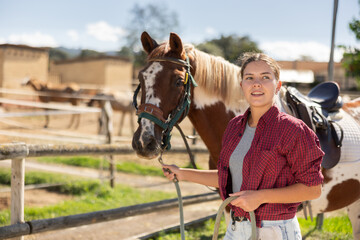 Young woman leading horse by bridle in paddock