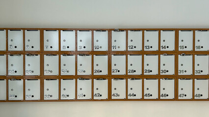 A row of numbered metal mailboxes mounted in a wooden frame on the wall. Each cell is equipped with a lock and a slot for mail. The organized structure and minimalist design create a neat and orderly 