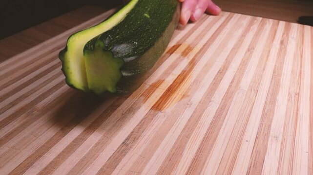 Chef slice zucchini with a closeview. Cutting long green courgettes in slow motion with a knife on a wooden board. Chopped courgette. Slow motion cooking video. Fresh italian salad with courgette. 