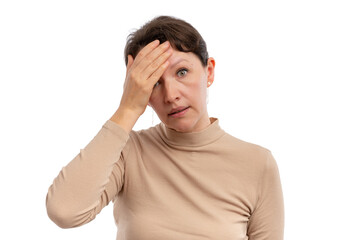 A woman with a worried expression, holding her forehead, wearing a beige turtleneck against a white...