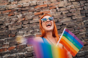 Happy activist waving rainbow flag celebrating lgbtq plus pride in front of brick wall