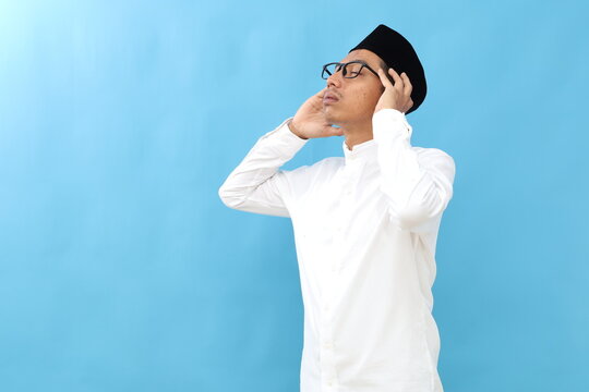 Young asian muslim man wearing moslem clothes and prayer while close eyes. He is on the call to prayer or adzan