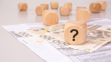 Wooden block with a question mark on financial documents and banknotes, symbolizing economic...
