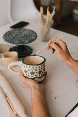 Artist is making decoration on the clay ceramic mug after oven firing. Design earthenware cup with a traditional pattern.