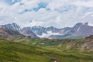 Scenic alpine landscape with green hills and rocks with view to big glacier and large snow-capped...