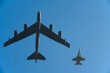 B-52 Stratofortress and fighter jet flying in formation against a clear blue sky. Ample copy space.