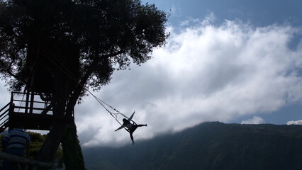 Silhouette of a person on the Swing at the End of the World, and of the tree with the treehouse at the Casa del Arbol, in Banos, Ecuador